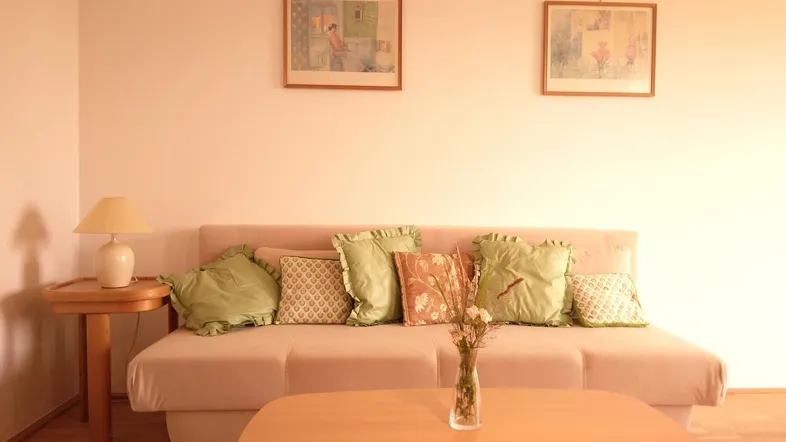 Helles Wohnzimmer mit beigem Sofa, Holzboden und zwei gerahmten Bildern an der Wand.