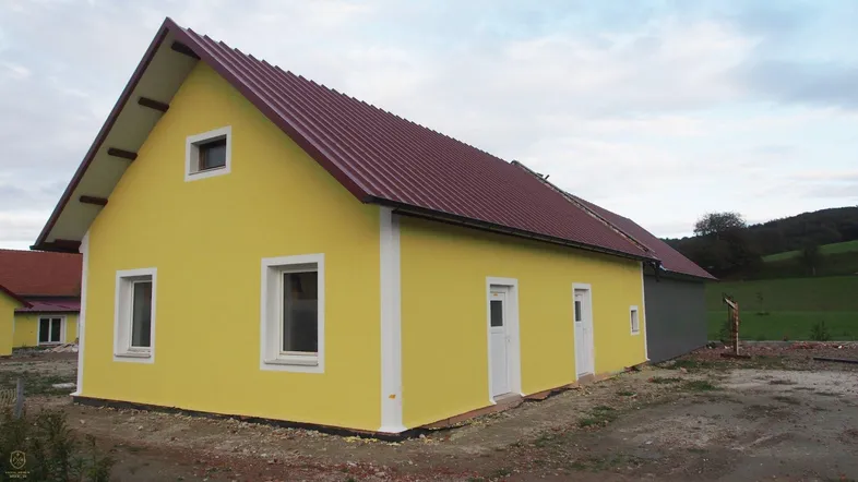 Gelbes Einfamilienhaus mit rotem Satteldach und weiß gerahmten Fenstern in ländlicher Umgebung.