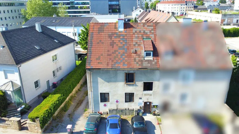 Luftaufnahme eines Wohnhauses mit rotem Ziegeldach und geparkten Autos davor in städtischer Umgebung.