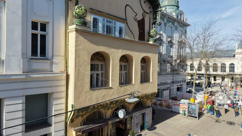 Historische Fassade eines Gebäudes mit kunstvollen Verzierungen und Blick auf eine belebte Einkaufsstraße.