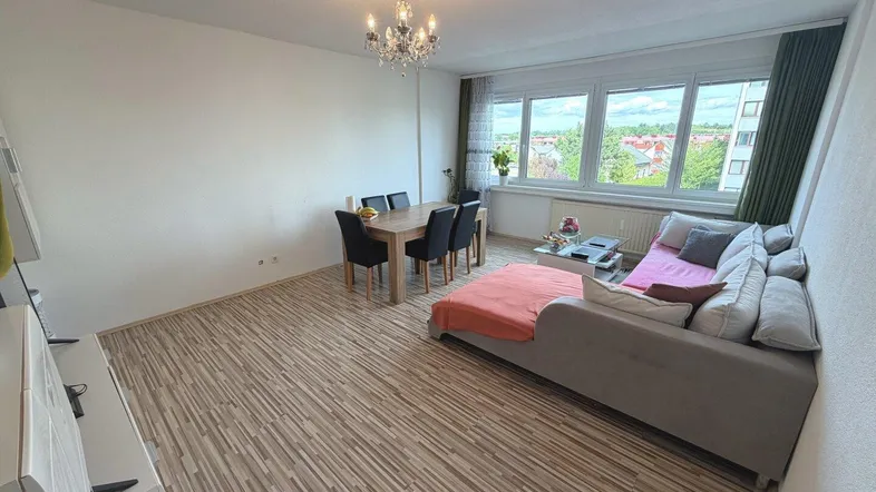 Helles Wohn- und Esszimmer mit Laminatboden, großem Fenster und Kronleuchter, bietet viel Tageslicht.