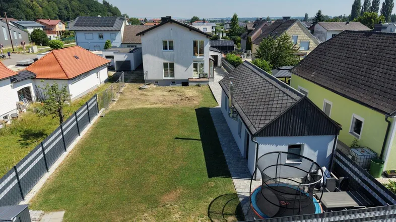 Gepflegter Gartenbereich mit Rasenfläche, Trampolin und Sitzgelegenheit hinter dem Haus.