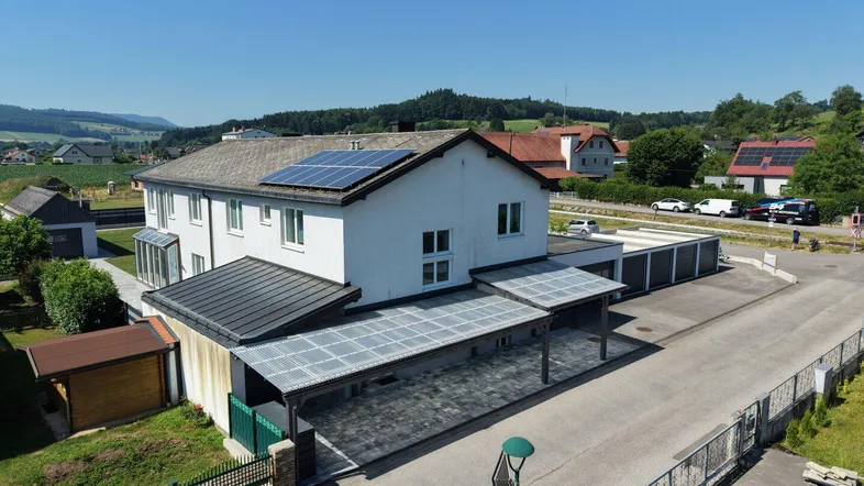 Luftaufnahme eines Hauses mit Photovoltaikanlage, Carports und ländlicher Umgebung.