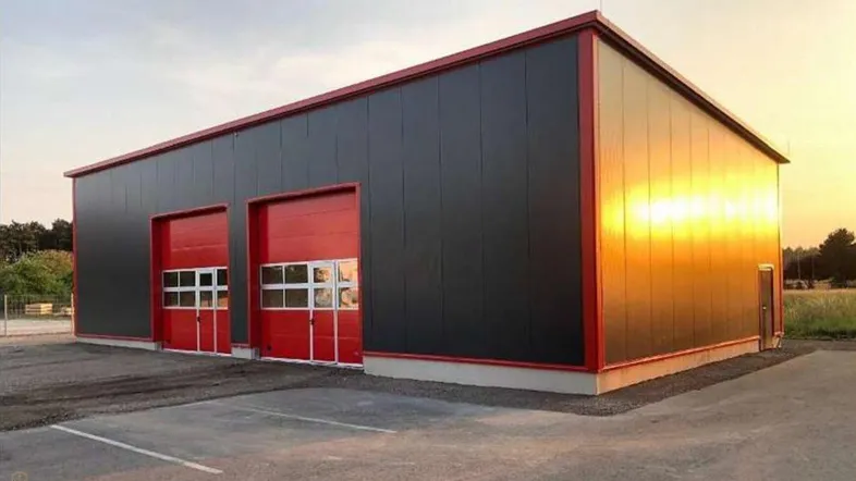 Modernes Industriegebäude mit dunkler Fassade und leuchtend roten Rolltoren, beleuchtet von der Abendsonne.