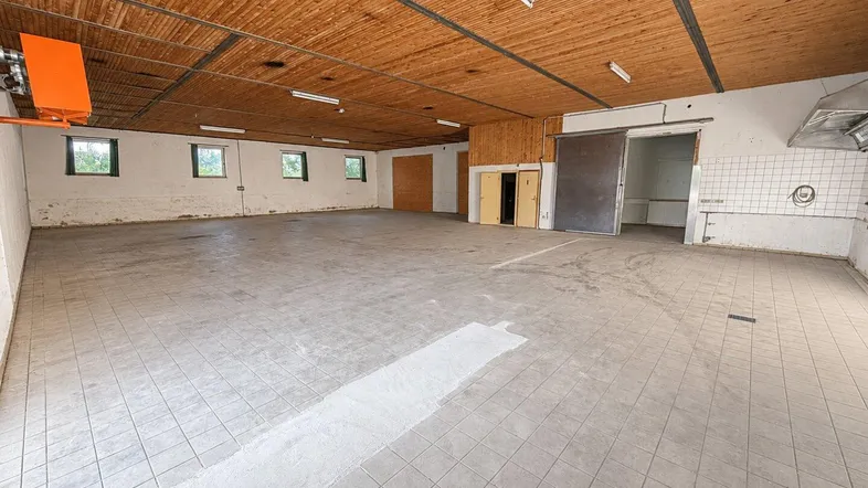 Großer, leerer Gewerberaum mit Holzbalkendecke, Fliesenboden und Fenstern, ideal für Lager oder Werkstatt.
