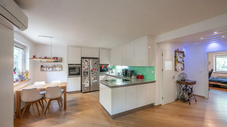 Moderne offene Küche mit weißen Hochglanzfronten, Essbereich und Holzboden.