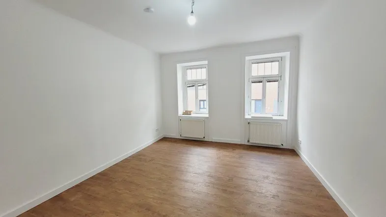 Helles, leeres Zimmer mit weiß gestrichenen Wänden und neuem Holzfußboden, bereit zur individuellen Gestaltung.