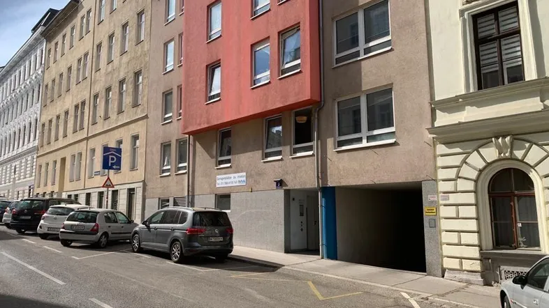 Gebäudefassade mit rotem Akzent und Eingang zur Tiefgarage von der Straße aus gesehen.