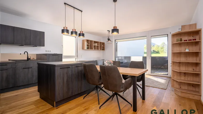 Moderner offener Wohn-Essbereich mit integrierter Küche, Holzboden und Zugang zum Balkon.