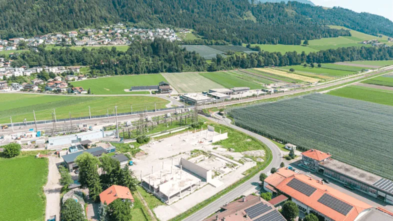 Luftaufnahme einer ländlichen Gegend mit Bergen, Feldern, Wohnhäusern und einer Baustelle.