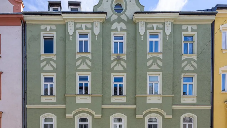 Historisches Mehrfamilienhaus mit grüner Fassade und klassischer Architektur unter blauem Himmel.