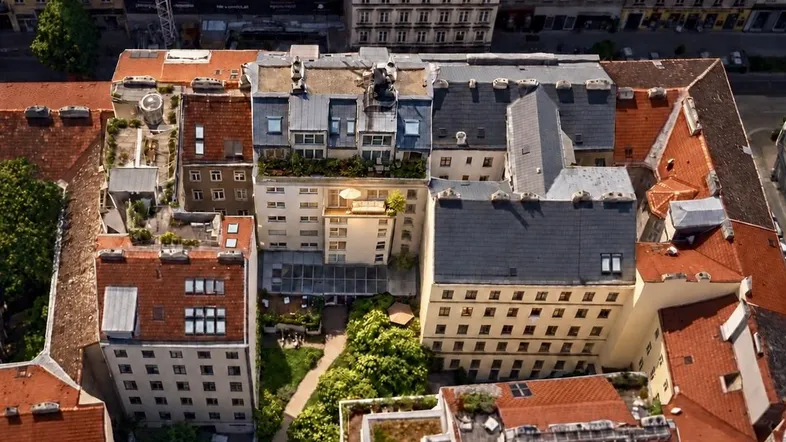 Luftaufnahme von Gebäuden mit begrüntem Innenhof und Dachterrassen in städtischer Umgebung.