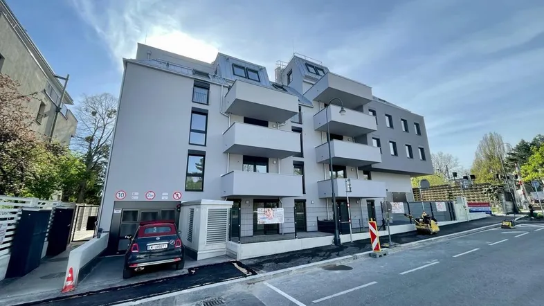 Modernes Mehrfamilienhaus mit Balkonen und Tiefgaragenzufahrt unter blauem Himmel.