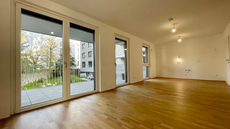 Helles Wohnzimmer mit Parkettboden, großen Fenstern und Zugang zu einem Balkon mit Gartenblick.
