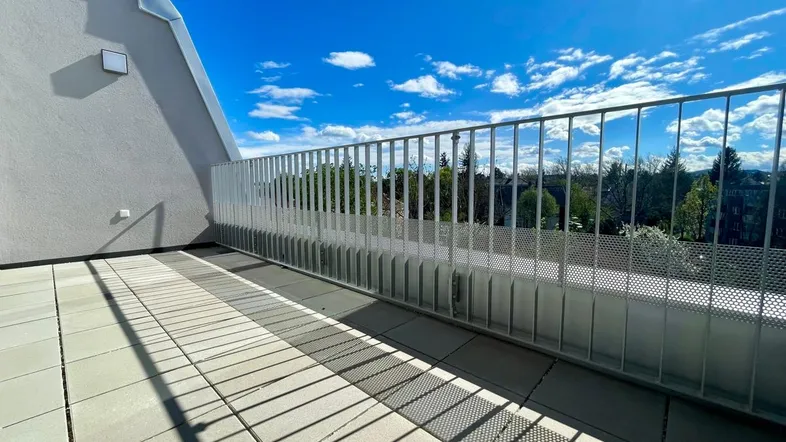 Geräumige Dachterrasse mit Fliesenboden und weitem Blick unter blauem Himmel.