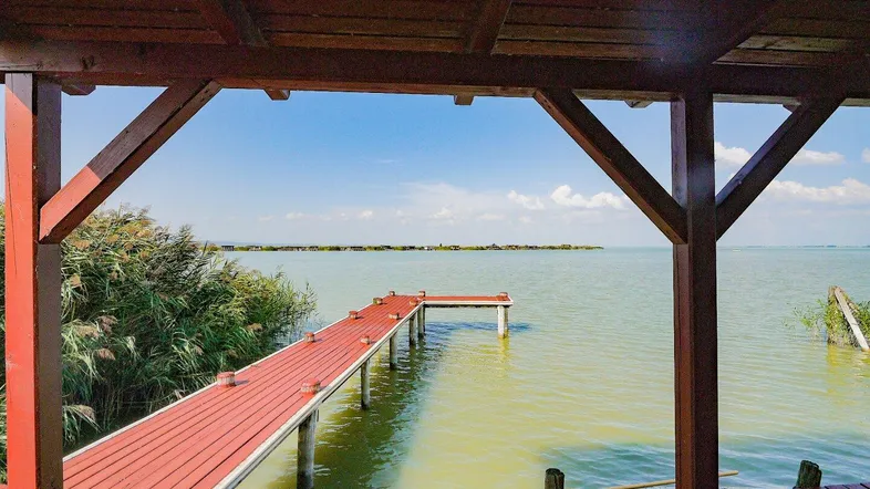 Überdachte Holzterrasse mit Blick auf den See und einen langen roten Steg.
