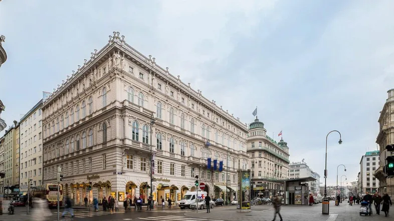 Historisches Gebäude an einer belebten Straßenkreuzung mit Fußgängern und Geschäften im Erdgeschoss.