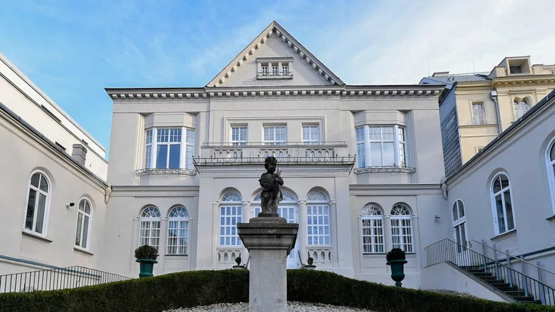 Elegantes historisches Gebäude mit klassischer Architektur, großen Fenstern und einem gepflegten Vorgarten mit Statue.