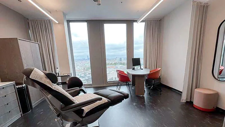 Modernes Behandlungszimmer mit bequemer Liege, Schreibtisch und weitem Blick über die Stadt.