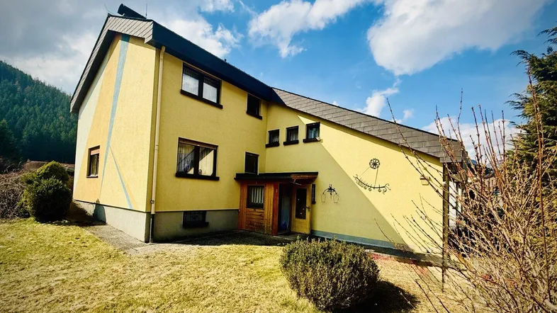Gelbes Einfamilienhaus mit schrägem Dach und dekorativen Elementen an der Fassade.