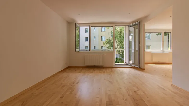 Helles Wohnzimmer mit Parkettboden, großen Fenstern und Zugang zum Balkon.
