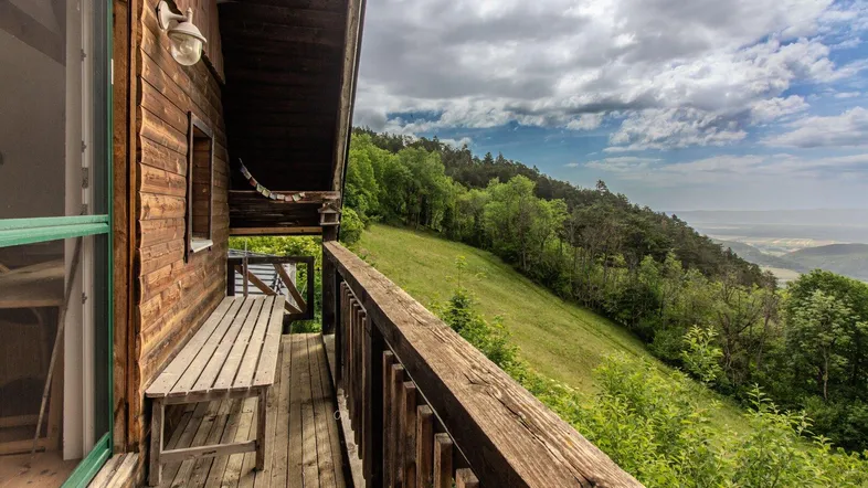 Rustikaler Holzbalkon mit Sitzbank und weitem Blick über die bewaldete Landschaft und das Tal.