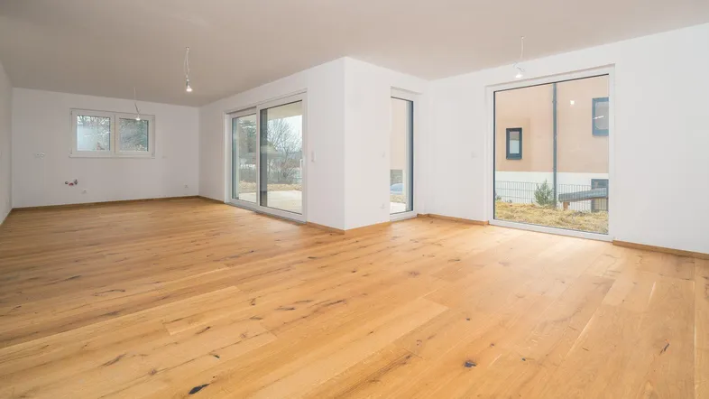 Heller, leerer Raum mit Holzboden und großen Schiebetüren, die viel Tageslicht hereinlassen.