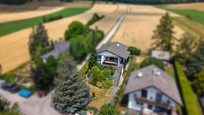 Luftaufnahme eines Einfamilienhauses mit Garten, umgeben von Feldern und ländlicher Landschaft.