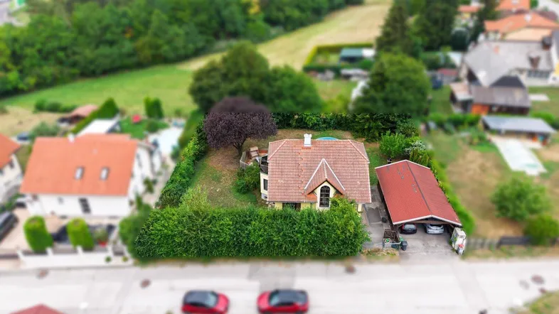Luftaufnahme eines Einfamilienhauses mit Garten, Carport und umliegender Wohnsiedlung.