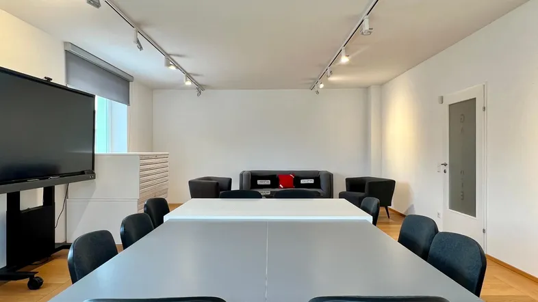 Geräumiger Konferenzraum mit großem Tisch, bequemer Sitzecke und moderner Beleuchtung für produktive Meetings.