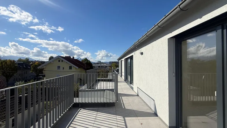 Langer, sonniger Balkon mit Fliesenboden und Metallgeländer, bietet einen weiten Blick auf die Umgebung.
