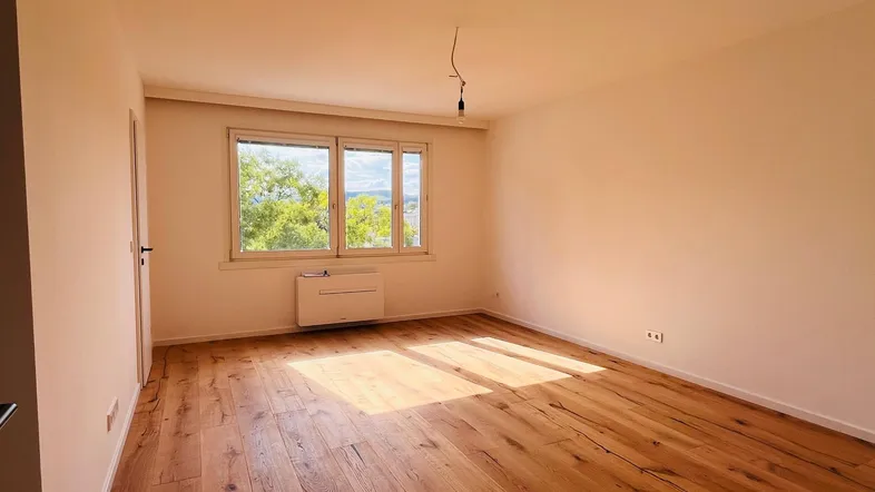 Helles Zimmer mit schönem Holzboden und Blick ins Grüne, ideal als Wohn- oder Schlafzimmer.