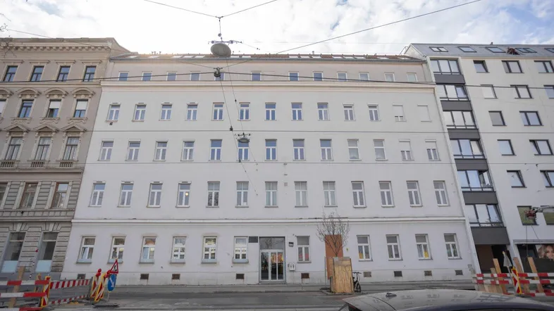 Klassisches Mehrfamilienhaus mit vielen Fenstern und einer hellen Fassade in städtischer Umgebung.