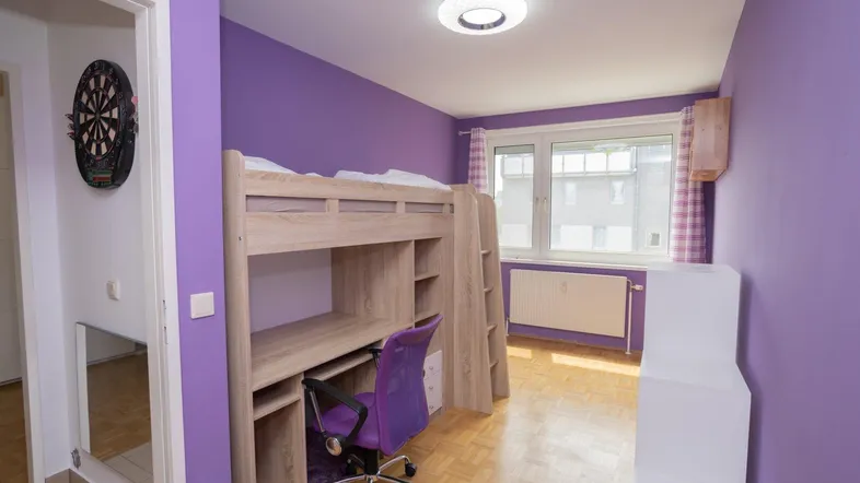 Kinderzimmer mit Hochbett, Schreibtisch und lila Wänden, hell und freundlich.