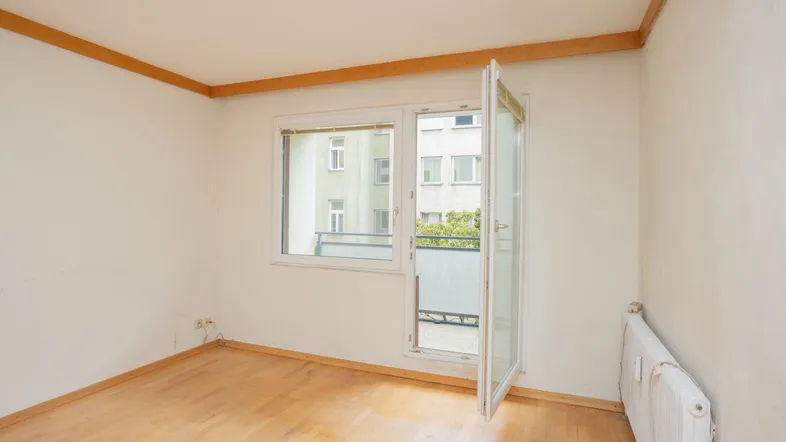 Helles Zimmer mit Holzboden und Zugang zu einem kleinen Balkon, bereit zur Einrichtung.