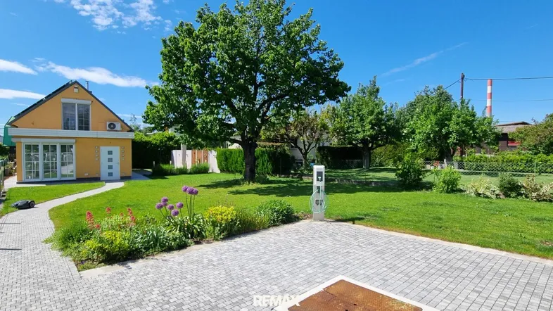 Haus mit Garten, gepflastertem Weg und Ladestation für Elektrofahrzeuge.