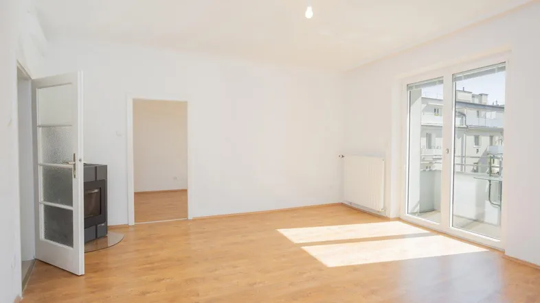 Helles Wohnzimmer mit Laminatboden, Kaminofen und Zugang zu einem sonnigen Balkon.