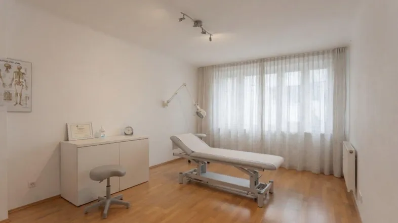 Helles Zimmer mit Holzfußboden und Behandlungsliege, ideal als Praxisraum oder Büro.