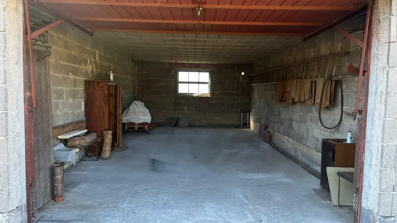 Geräumige Garage mit Betonwänden und -boden, einem kleinen Fenster und offenem Tor, ideal als Lagerraum.