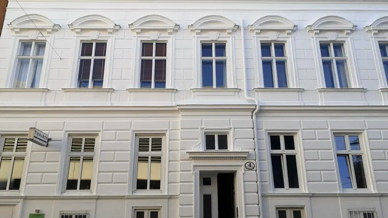 Klassische weiße Fassade eines Altbaus mit vielen Fenstern und dekorativen Stuckelementen, gut gepflegt.