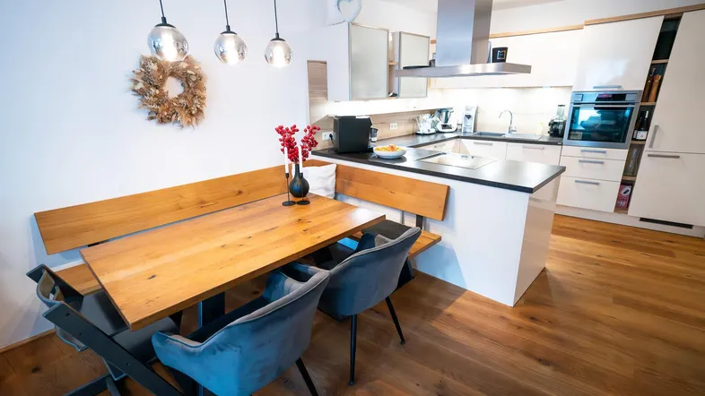 Moderne offene Küche mit Essbereich, Holztisch und integrierten Geräten, ideal für gesellige Mahlzeiten.