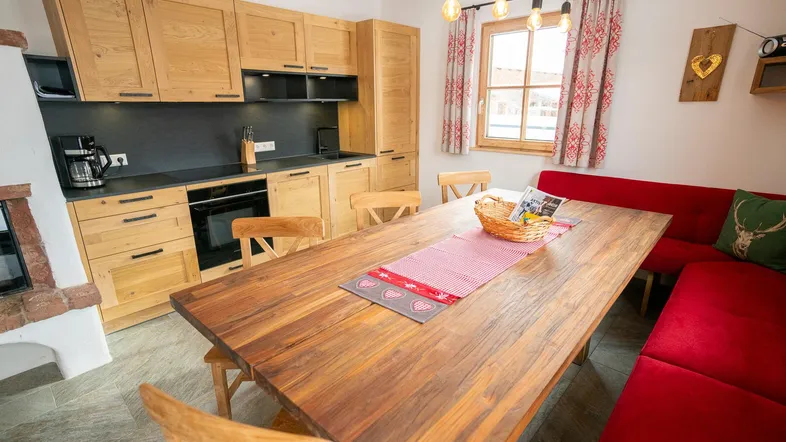 Gemütliche Küche mit Holzelementen, Esstisch und roter Sitzbank, ideal für gemeinsame Mahlzeiten.