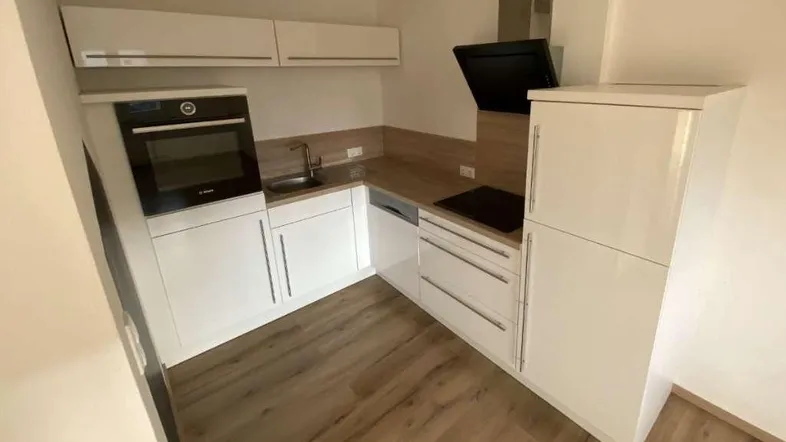 Moderne Einbauküche mit weißen Hochglanzfronten, Holzoptik-Arbeitsplatte und integrierten Geräten.