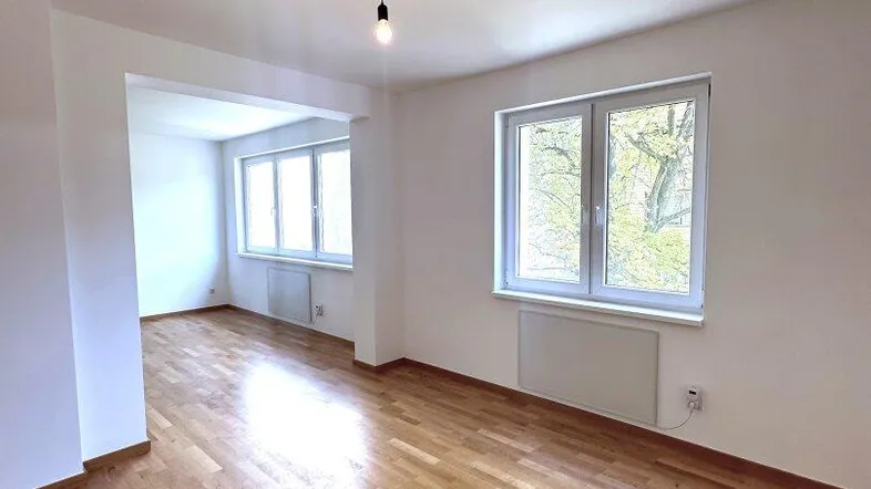 Helles Wohnzimmer mit Parkettboden und großen Fenstern, die viel Tageslicht hereinlassen.