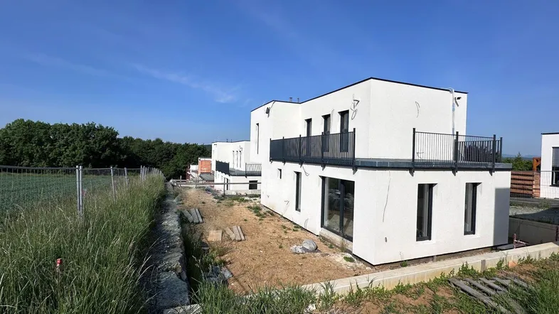 Moderne weiße Neubauhäuser mit Balkonen in einer ländlichen Umgebung unter blauem Himmel.