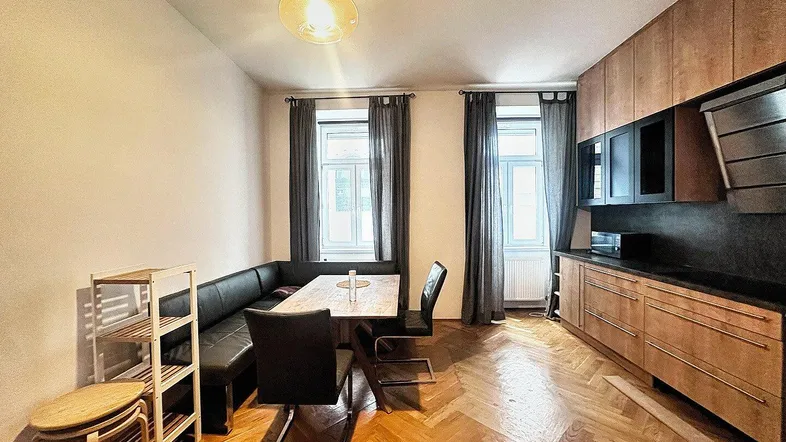 Geräumige Wohnküche mit Holzboden, integrierter Küchenzeile und Essbereich am Fenster.