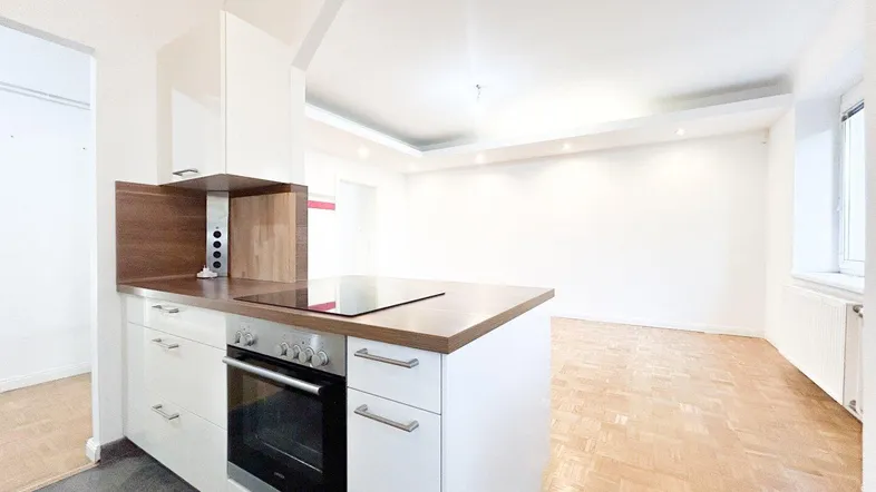 Moderne Küche mit Kochinsel, Backofen und Induktionskochfeld, offen zum Wohnbereich mit Parkettboden.