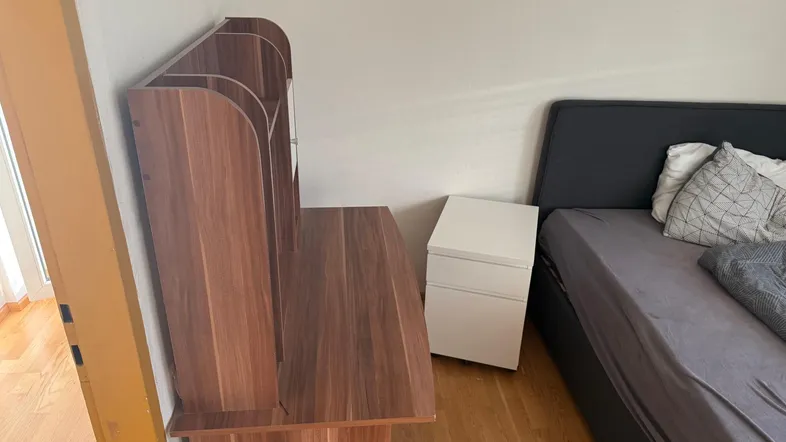 Schlafzimmer mit Holzboden, einem Bett mit dunklem Kopfteil und einem Nachttisch.