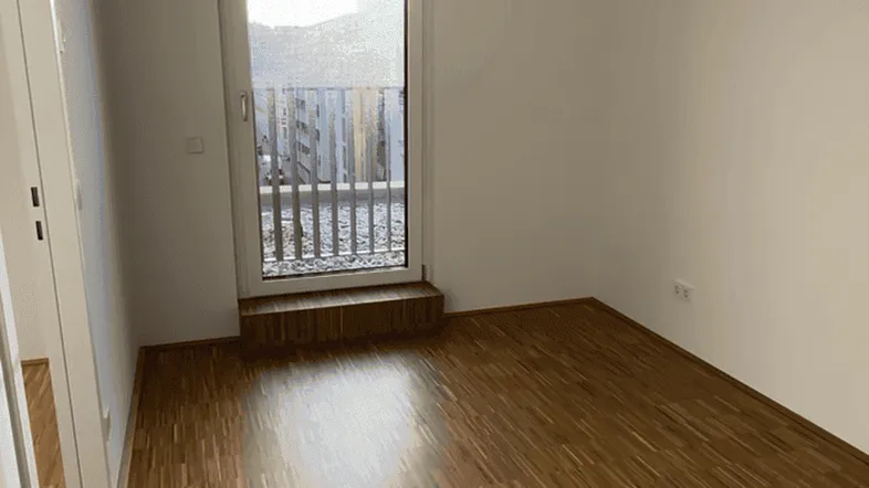Helles Zimmer mit Holzboden, Klimaanlage und Zugang zu einem kleinen Balkon.