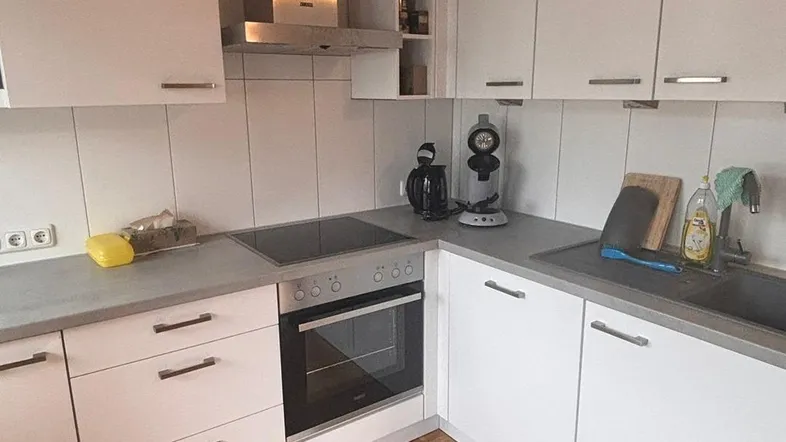 Moderne Küche mit weißen Schränken, dunkler Arbeitsplatte und Parkettboden unter Holzbalken.